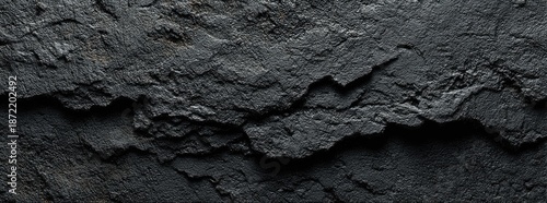 Close-up of rough, dark grey rock surface with deep fissures and textured details