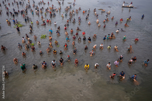 Pabna, Bangladesh - 05 December 2020: Aerial view of people wading in the shallow, reflective waters, their figures creating a mosaic of humanity against the muted tones of the landscape.