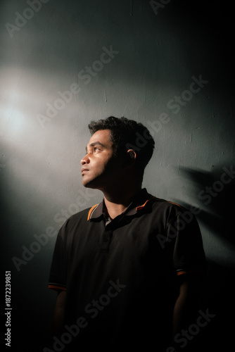 Fotografi A young man looking up towards a light beam with a hopeful expression
