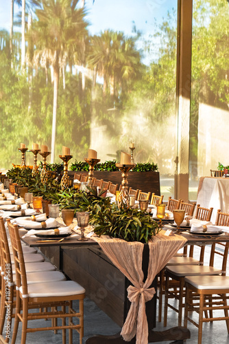 Wedding reception in Florida featuring elegantly decorated tables in white and gold style, palm trees in the background and bright sunshine. Tropical outdoor wedding, luxury celebration