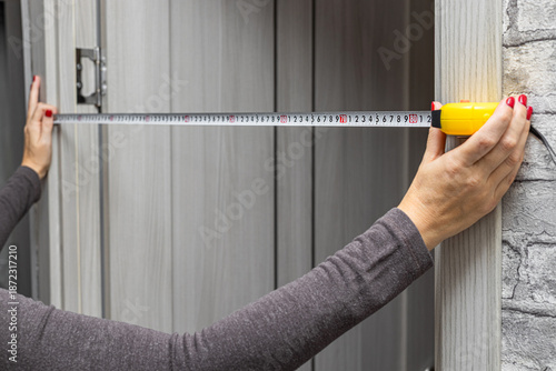A woman measures a doorway with a tape measure. a measuring tape in a woman's hands. woman doing home renovations. a measuring tape in a woman's hands