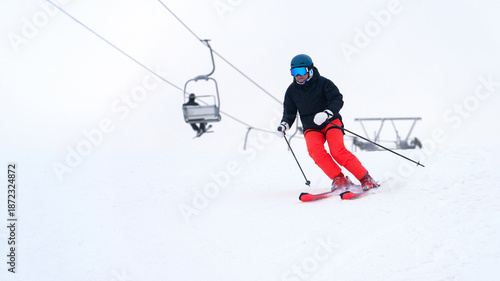 A skier moves along a white snowy slope at a ski resort, with a chairlift in the background. Snow flies out from under his skis.