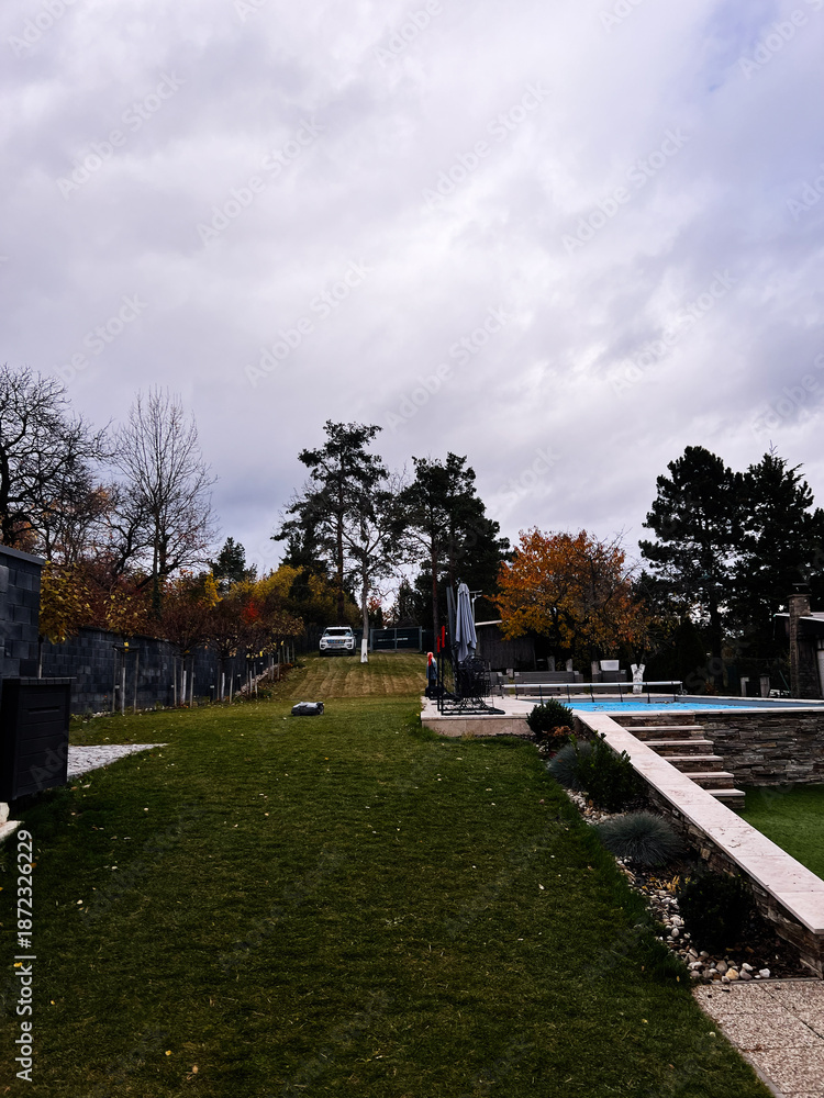 Fototapeta premium Relaxing backyard with pool, lounge area, and autumn trees in a peaceful yard