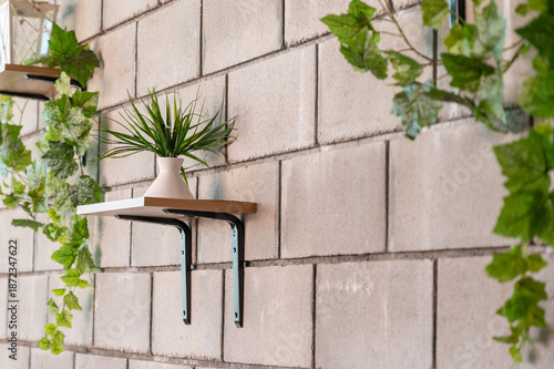 Stylish home interior detail. Concrete brick wall with wooden shelves and decorative greenery.