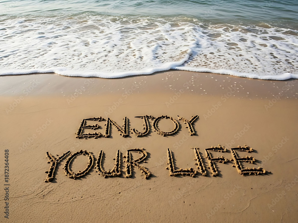 Fototapeta premium Enjoy your life message written in sand on a beach by ocean waves