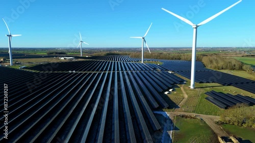 Aerial view of Chelveston Wind Farm showcasing solar panels contrasting with lush green fields and wind turbines against a clear blue sky, Chelveston, Wellingborough, United Kingdom.
