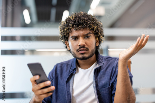 Foto Close-up photo of a young Indian man holding a phone in his hand, looking at the