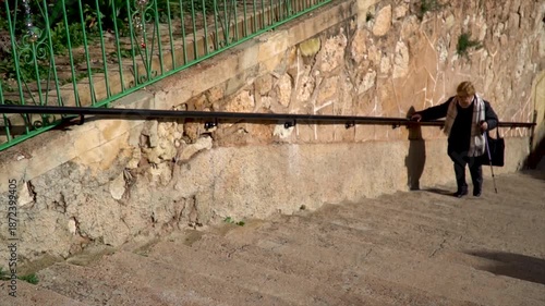 An elderly woman climbing a staircase while holding onto the railing.
