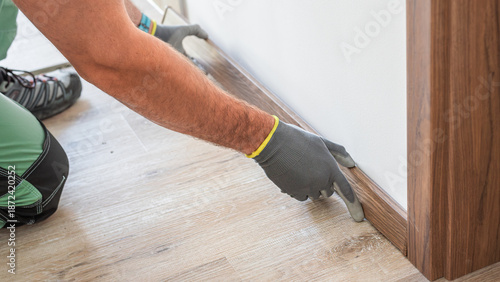 Installing elegant plastic baseboard, showcasing skilled craftsmanship in home improvement and renovation. Detailed view of pro floating floor work, fitting trim for seamless interior finish.