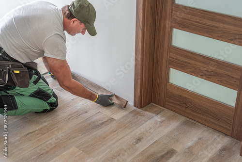 Installing elegant plastic baseboard, showcasing skilled craftsmanship in home improvement and renovation. Detailed view of pro floating floor work, fitting trim for seamless interior finish.