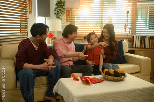 Asian family sitting together on the sofa during Chinese New Year, smiling and enjoying watching television while sharing a warm holiday moment at home