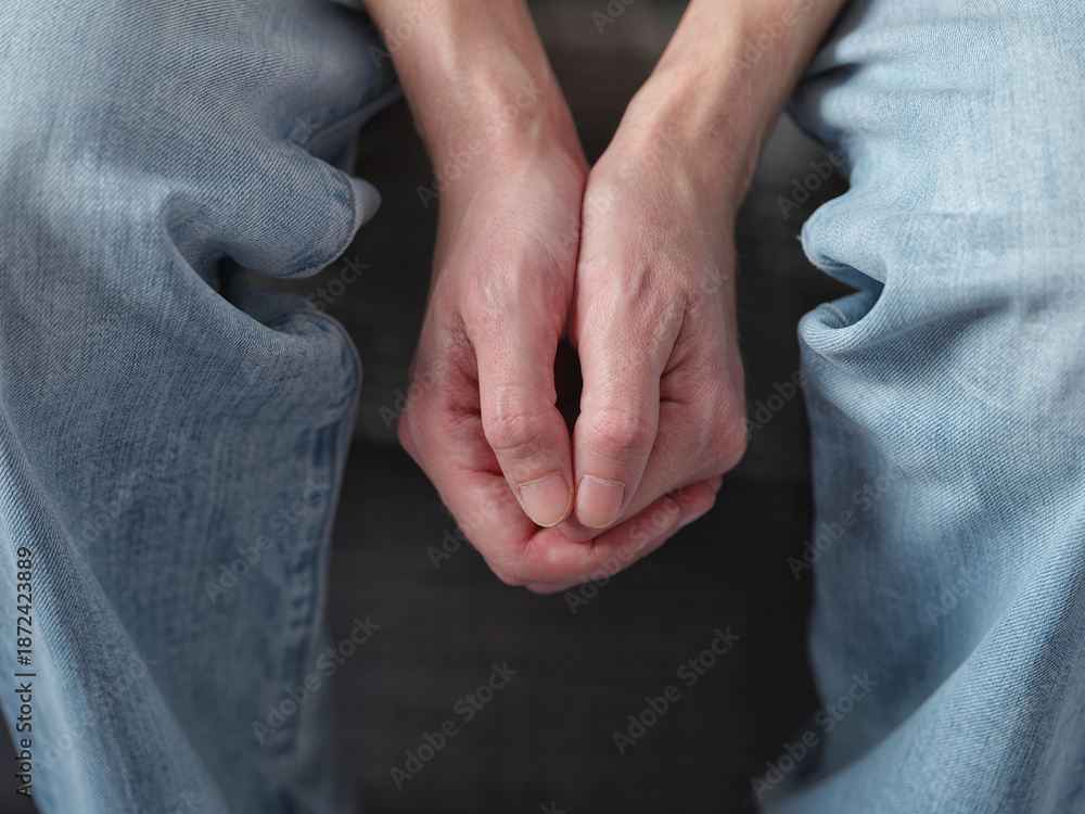 Fototapeta premium A man clasping his hands together in his lap, conveying emotions of anxiety, stress, or contemplation. Close up.