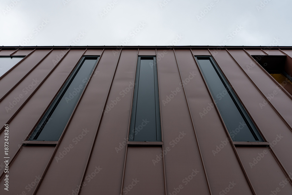 Obraz premium Vue en contre-plongée d’une façade contemporaine en bardage métallique brun avec ouverture architecturale, illustrant un design moderne et minimaliste.
