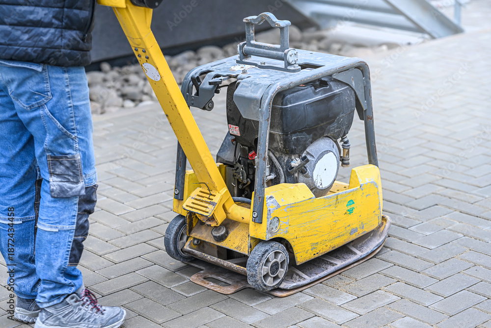 Fototapeta premium Working with vibro-compaction plate to compact self-locking blocks in their laying bed. Vibrating plate in construction.