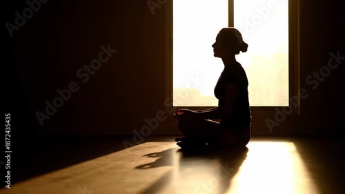 Silhouette woman meditating by window in warm morning light