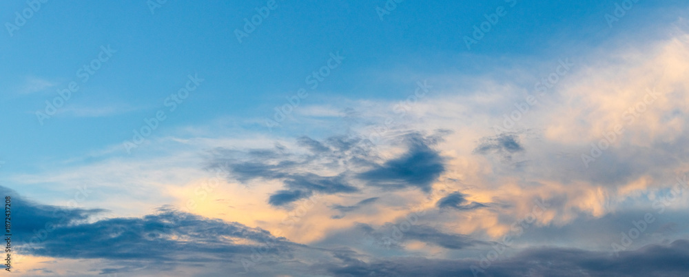 Fototapeta premium Bright blue sky with delicate clouds and warm golden-pink hues at sunset