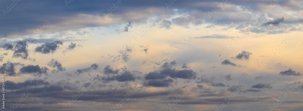 Obraz premium Panoramic view of evening sky with soft golden sun rays and scattered dark blue clouds during sunset