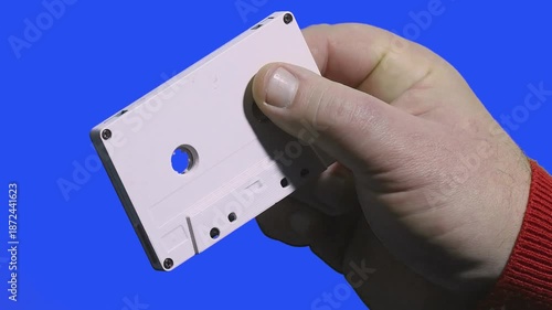 Compact audio cassette shown on blue background with hand holding it
