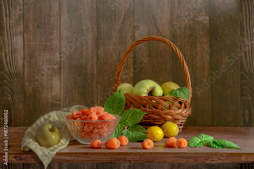 A delicious still life with orange raspberries and green apples in a basket