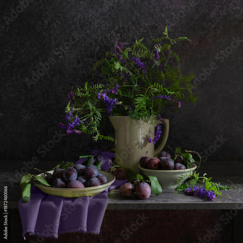 Still life with a plate of plums, a jug with a bouquet of wild flowers in blue-lilac and gray-black tones