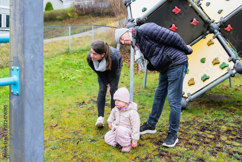 Photography Family members, a woman and a man, are observing a young child playing on a play