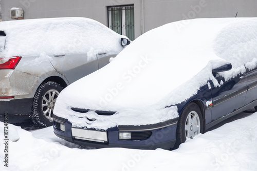 Cars under the snow after a snowfall. Fresh white snow on the roofs, windows and hoods of cars. Closeup.
