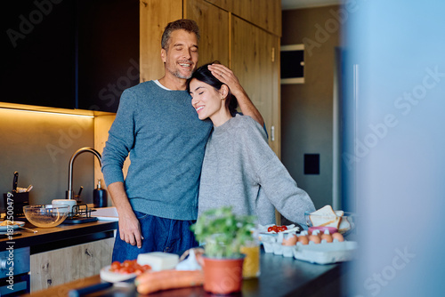 Tableau sur toile Loving couple standing together in a modern kitchen, sharing a tender moment and