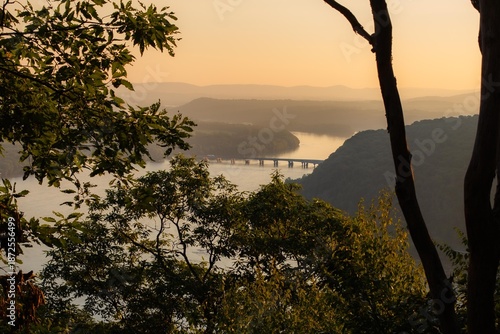 Golden sunset over winding river and forested hills, scenic landscape with bridge
