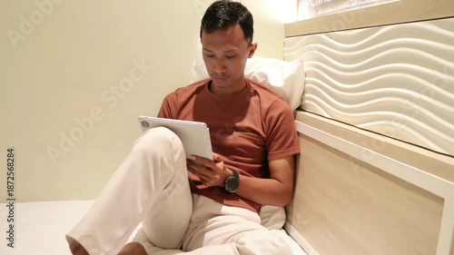 An Asian man using a tablet in bed