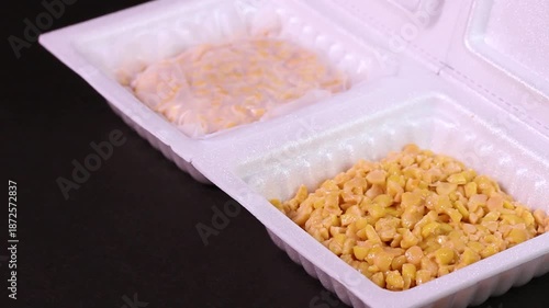 黒背景で回転するパック入りのひきわり納豆（フィルム付きと中身）