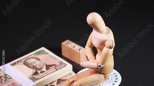 黒背景で回転する札束とTAXの文字ブロック、木製人形（税金・確定申告イメージ）