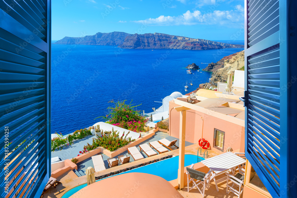Obraz premium Sea view past blue window shutters of pastel and whitewashed terraces and houses at the idyllic Greek village of Oia, on the island of Santorini, Greece.