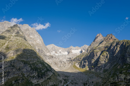 Expansive view of the Glacier de Triolet surrounded by steep, rocky mountain faces and dramatic shadows beneath a vibrant, cloudless sky in the Mont Blanc massif.
