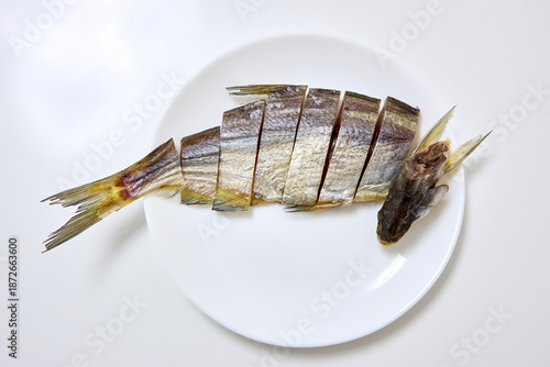 A top-down shot showcases sliced dried fish arranged on a white plate over a white background, emphasizing Asian culinary arts and conventional food preparation methods.