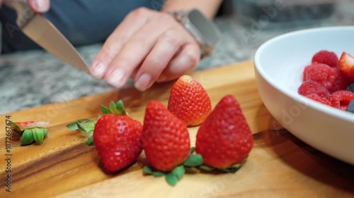 close up of person slicing fresh strawberries on a wooden board for a mixed fruit bowl