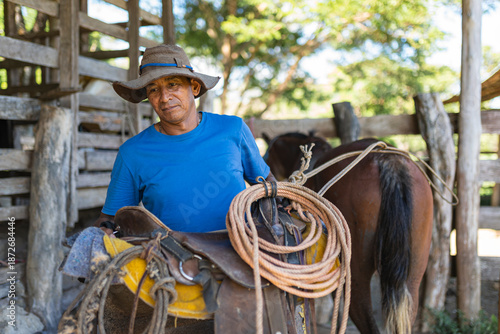 Costa Rican cowboy carrying saddle and lasso in rustic stable