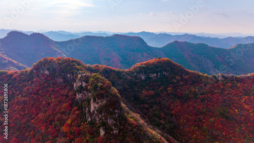 Autumn red leaves blanket the mountains, creating a continuous layer of forest colors. The aerial view reveals a continuous range of layered mountain scenery