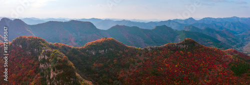 Autumn red leaves blanket the mountains, creating a continuous layer of forest colors. The aerial view reveals a continuous range of layered mountain scenery