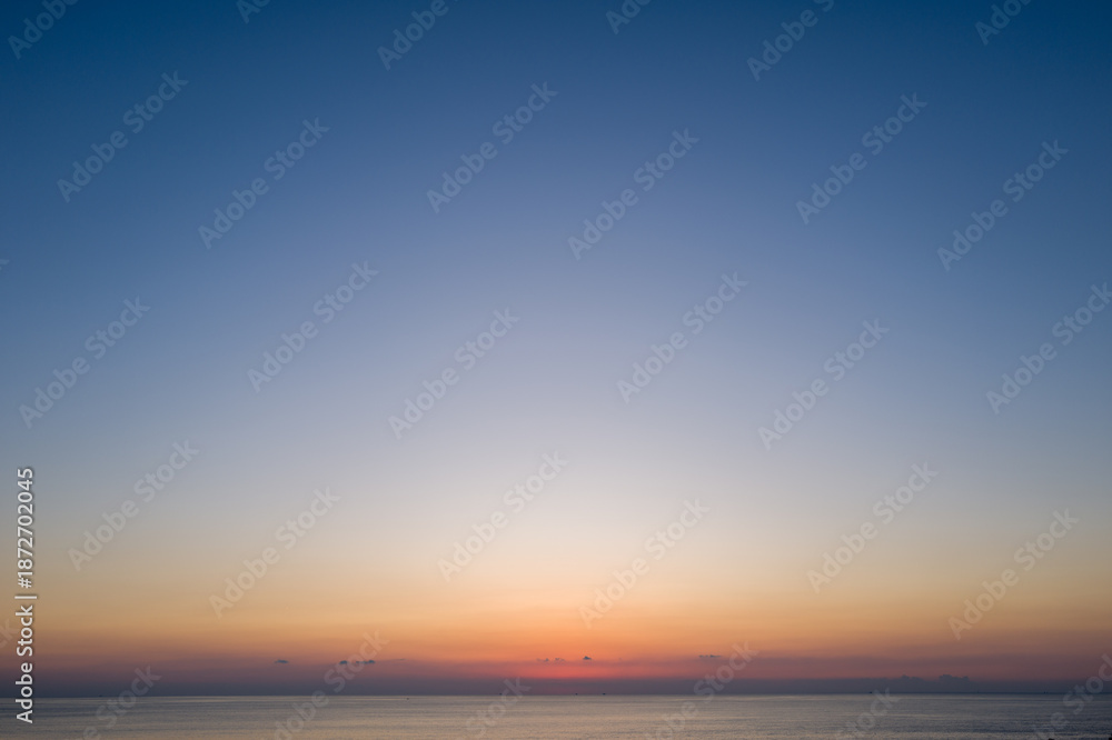 Obraz premium Expansive view of the calm sea beneath a wide open sky, fading from deep blue to warm orange hues at sunset in Kushimoto, Japan.