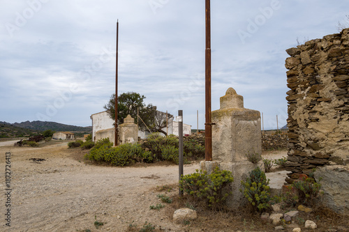 Fotografía Two weathered stone gateposts with rusted metal poles stand at the entrance of a deserted village in Asinara National Park, Sardinia