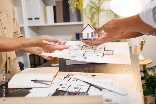 
Two people are working on a house plan design. They are using various tools, working with the plan, and reviewing a house model to verify the accuracy of their work in the workplace.

