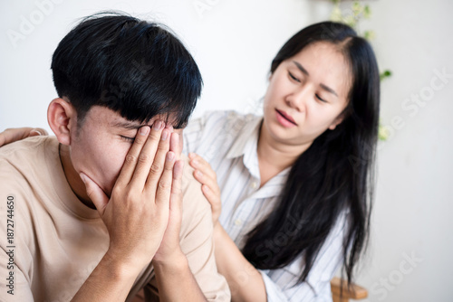 Fotografie A worried young woman comforting a stressed Asian man covering his face in despair