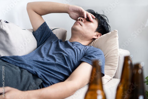 Bild auf Leinwand Exhausted Asian man lying on a sofa feeling sick with a hangover after drinking beer