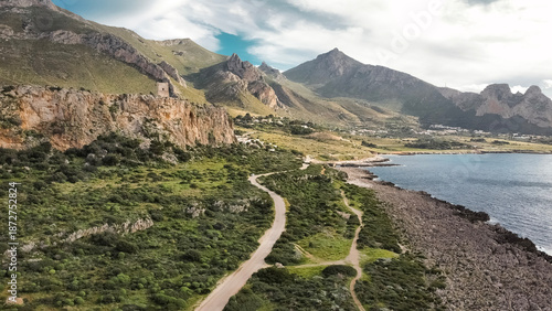 Aerial View Of San Vito Lo Capo In Sicily: Coastal Road Winding Through Green Mediterranean Landscape Toward Southern Rock Climbing Cliffs And Limestone Mountains