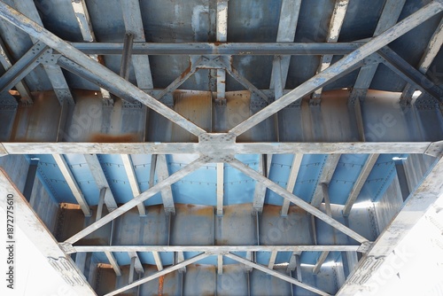 Detailed perspective of the weathered underside of a blue steel bridge