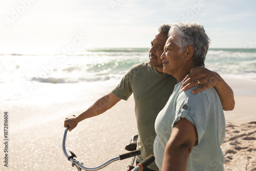 Thoughtful multiracial senior couple looking away while standing with bicycles at sunny beach
