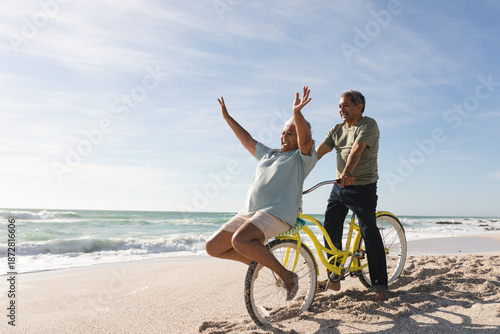 Cheerful senior multiracial couple enjoying retirement with bicycle at beach on sunny day