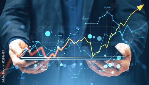 Businessman holding tablet with financial charts and upward arrow showing growth and investment trends on abstract digital background.