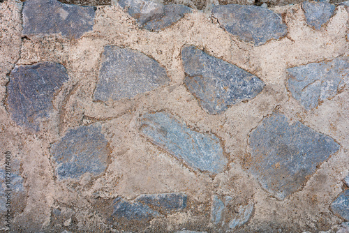 Close up of a weathered stone wall surface with irregular blue gray rocks set in light brown mortar
