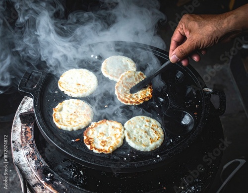 Sizzling Culinary Craft: Close-up shot of a hand flipping golden arepas cooking on a hot pan and steam